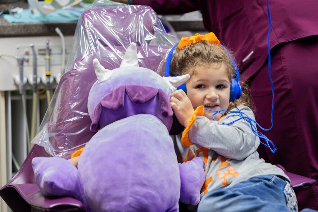 A young girl in Kansas relaxes during a dental appointment, using headphones and a plush toy for comfort—demonstrating how inclusive dental practices support patients with intellectual and developmental disabilities.