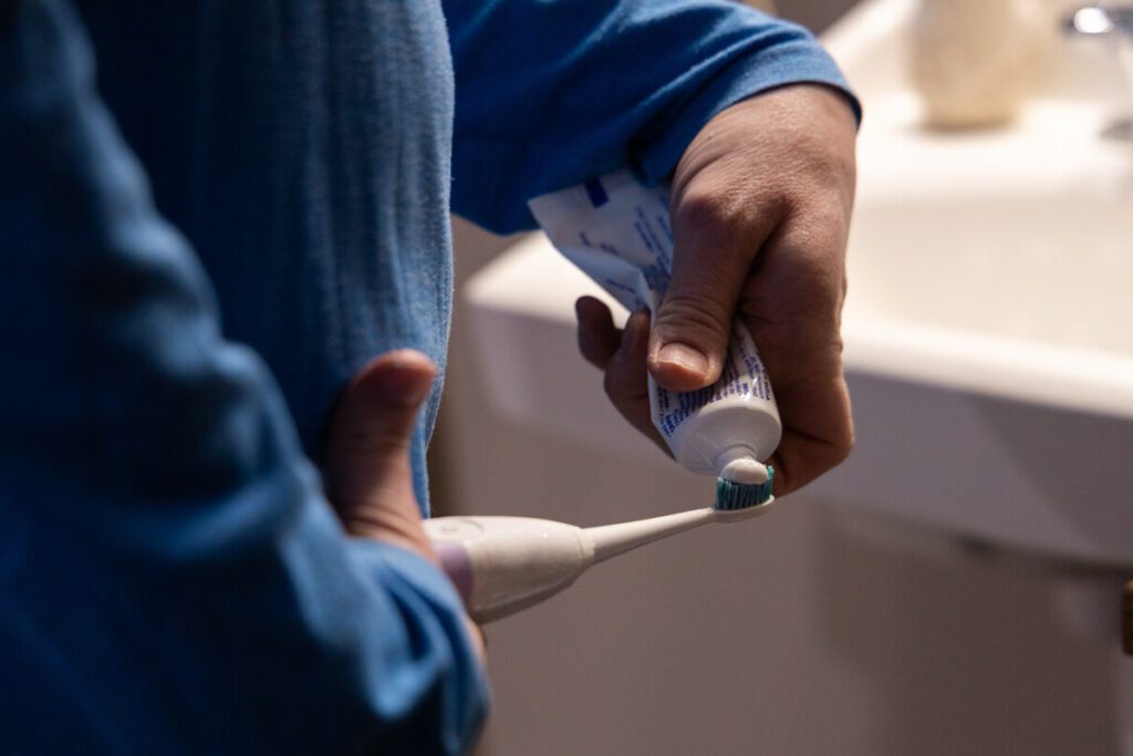 A person in Kansas applies toothpaste to an electric toothbrush, highlighting daily oral hygiene practices promoted through inclusive educational tools for people with disabilities and their caregivers.